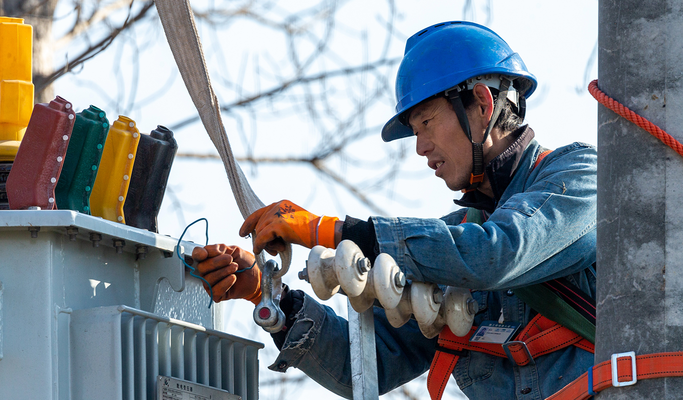 该项工程旨在完善农田灌溉电力设施，为即将到来的春灌提供稳定可靠的电力保障。图2为，2026年1月8日上午，在河南省安阳市滑县半坡店镇杏头村的农田里，杏头5号机井通电配套工程施工现场，国网滑县供电公司施工队员霍俊英正在对吊装的变压器进行脱钩作业。（王亚方 摄）
