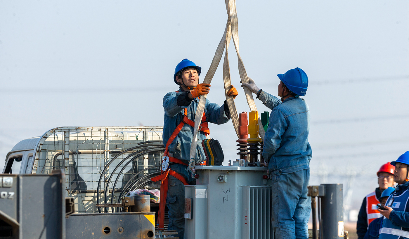 国网滑县供电公司将继续加快推进工程进度，确保所有设施在春灌前投入使用，切实服务农业生产。图7为，2026年1月8日上午，在河南省安阳市滑县半坡店镇杏头村的农田里，杏头5号机井通电配套工程施工现场，施工队员正在准备起吊变压器。（王亚方 摄）