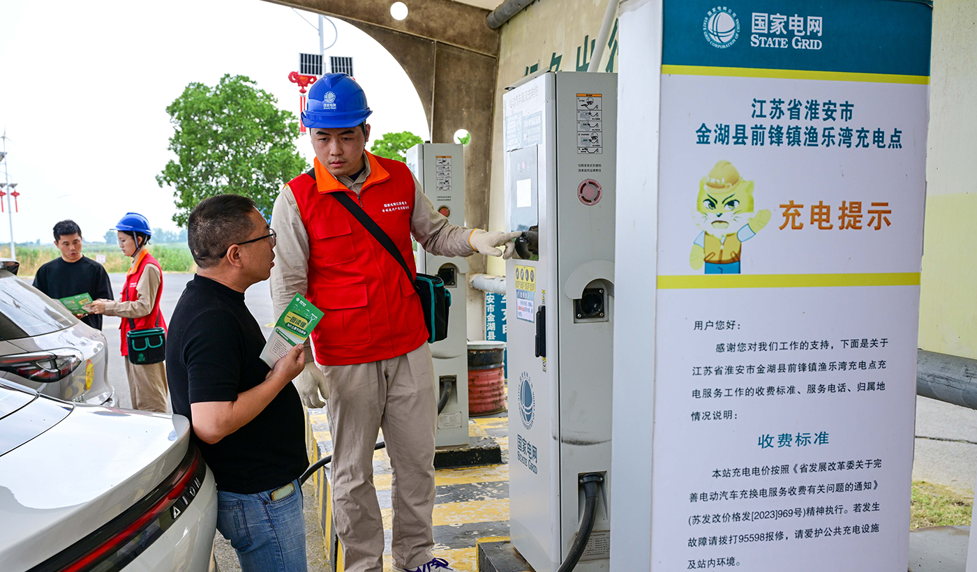 6月15日江苏省淮安市金湖县前锋锋镇渔乐湾充电站，电暖流党员服务队队员吴继文、朱凌宇向正在充电的电动车主宣传分时段充电政策。 